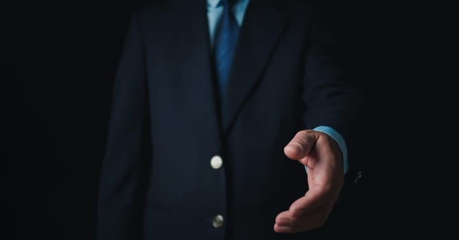 Businessman standing and doing handshake gesture on dark background. Business concept. Copy space.