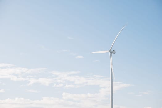 A picturesque angle of windmill turbines on a mountain farm embodies clean energy innovation. The modern wind industry drives sustainable development against the backdrop of a clear blue sky.
