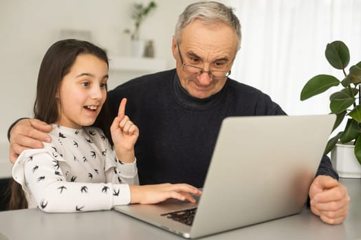 Portrait of senior man and young girl granddaughter using laptop at home