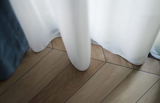White curtain touching floor with parquet board at home closeup. Interior design concept