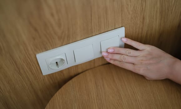 Hand pressing light switch in wall of house closeup. Saving electricity concept