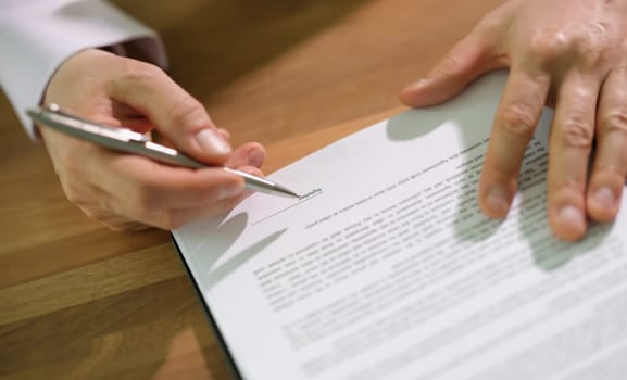 Hands of businessman with pen signing contract document at table closeup. Official certification of important papers concept