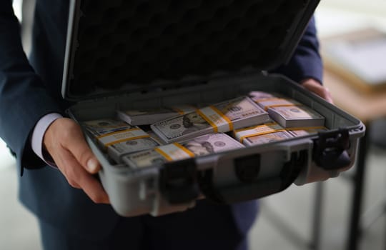 Banker holding suitcase with many dollar bills closeup. Crime and fraud giving bribe on large scale concept
