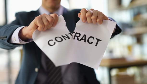 Businessman in suit tearing paper document contract at work in office closeup. Broken or breached contract violation of labor obligations concept