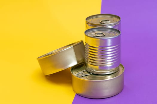 A Group of Stacked Tin Cans with Blank Edges on Split Yellow and Violet Background. Canned Food. Different Aluminum Cans for Safe and Long Term Storage of Food. Steel Sealed Food Storage Containers