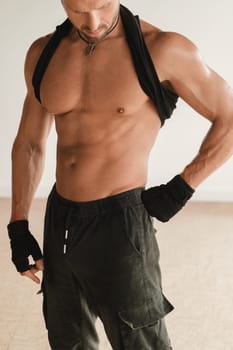 An adult muscular man with a naked torso stands in a room on a light background.