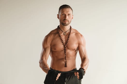 A man with a naked torso is engaged in strength fitness using a rubber loop indoors.