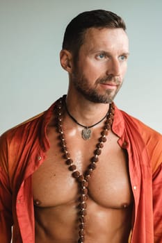 A muscular man with a naked torso in orange clothes stands in a room on a light background.