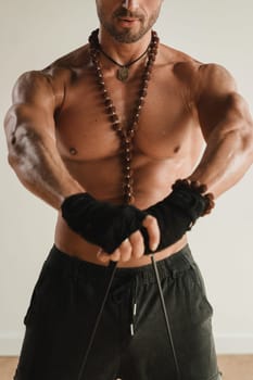 A man with a naked torso is engaged in strength fitness using a rubber loop indoors.