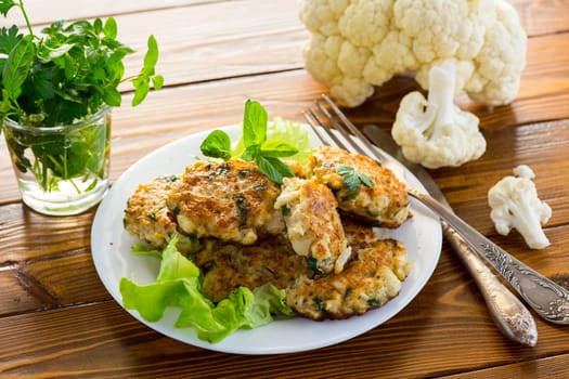 cooked vegetarian fried cauliflower cutlets, in a plate on a wooden table.
