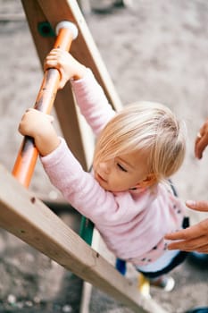 Mom supports a little girl climbing the stairs in the playground. Cropped. High quality photo