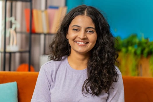 Portrait of happy calm Indian woman at home couch smiling friendly, glad expression looking away dreaming resting, relaxation feel satisfied good news, celebrate win. Arabian young girl in living room