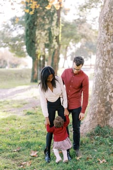 Mom holding hands a little girl standing with dad near the tree. High quality photo