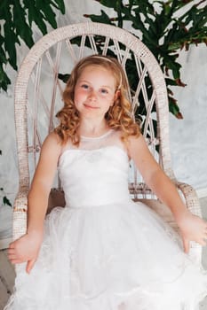 Beautiful fashionable girl in dress sits in a white chair by a tree
