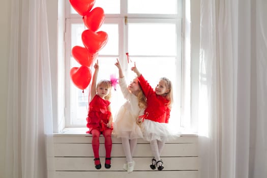 three little girl girlfriends in red and white dresses by the window