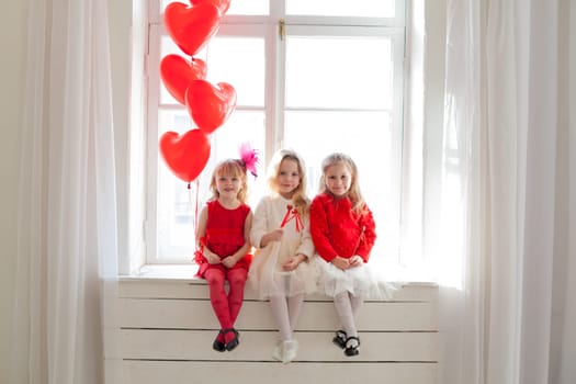 three little girl girlfriends in red and white dresses by the window