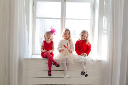three little girl girlfriends in red and white dresses by the window