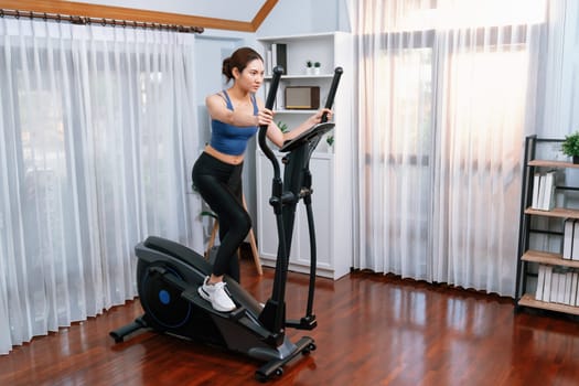 Energetic and strong athletic asian woman running on elliptical running machine at home. Pursuit of fit physique and commitment to healthy lifestyle with home workout and training. Vigorous