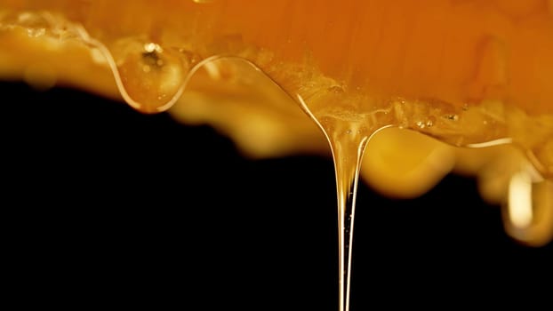 Honey dripping from honeycombs extreme macro.Natural beeswax cells, gold nectar. Organic liquid dessert pouring on black background. High quality