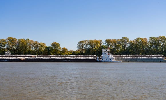 Large tug boat pushing rows of barges with grain products up the Mississippi river south of Cairo in Illinois