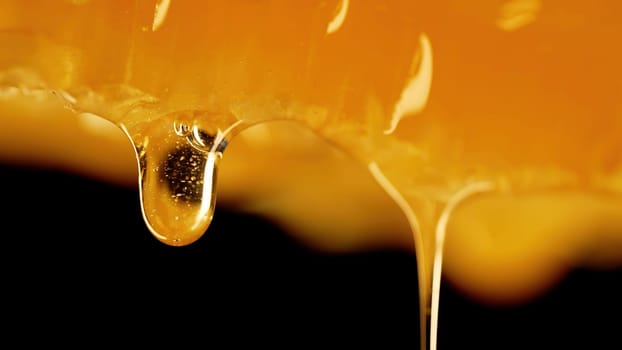 Honey dripping from honeycombs extreme macro.Natural beeswax cells, gold nectar. Organic liquid dessert pouring on black background. High quality