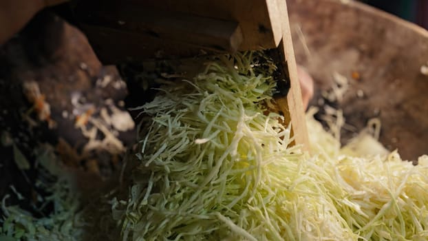 Woman rubs cabbage on grater, cooking traditional ukrainian fermented - sauerkraut salad from shredded carrot. Mixes chopped vegetables in family's ancient wooden trough. High quality