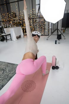 Engaged in sports activities with a virtual reality headset, dressed in stylish pink sportswear by a Christmas tree. High quality photo