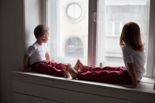 little boy and girl sitting by the window without parents