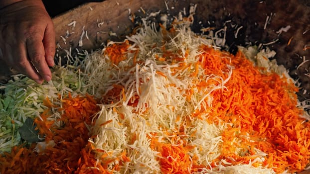 Woman cooking traditional ukrainian fermented - sauerkraut salad from shredded cabbage and carrot. Mixes chopped vegetables in family's ancient wooden trough. High quality