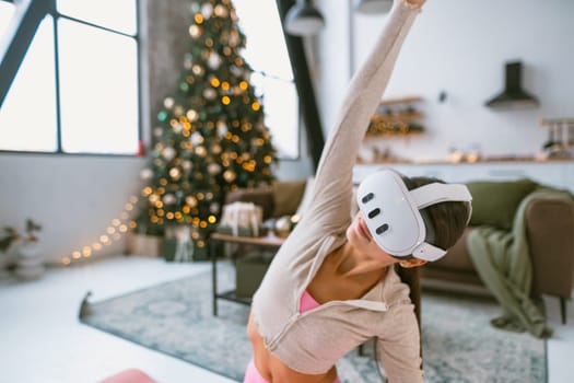 Practicing yoga poses, a fit young woman wears virtual reality glasses next to a Christmas tree. High quality photo