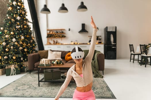 Engrossed in yoga practice, a fitness enthusiast wears virtual reality goggles by a Christmas tree. High quality photo