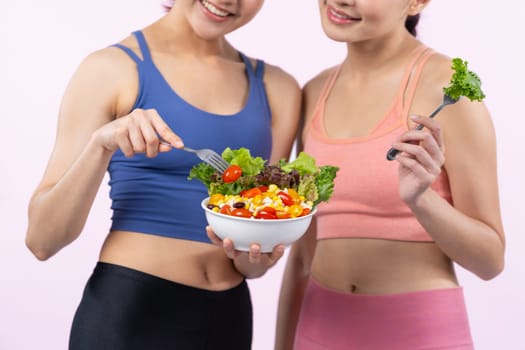 Two young sporty Asian women in sportswear holding salad bowl fill with fruit and vegetable. Natural youthful and fit body lifestyle people with balance nutrition on isolated background. Vigorous