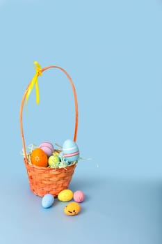 Easter basket filled with decorative multi colored eggs on a light blue background.Vertical