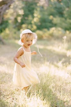 Little smiling girl in a panama hat walks through a sunny meadow. High quality photo