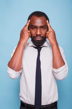 Unhappy black businessman contemplating office business problems and concentrating on solutions. Tired multiracial office worker relieves stress by pressing temples with index fingers.