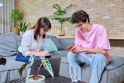 Young positive guy at therapy meeting with psychologist, patient and therapist sitting on sofa in office. Psychology, psychotherapy, treatment, mental health of youth concept