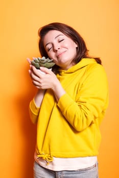 Portrait of woman snuggling up to succulent plant in a studio, demonstrating her passion for indoor plants. Young person petting and admiring the green leaves of potted decoration plant.