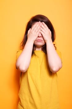 Troubled woman covering face and eyes with palms. Female person standing with hands on closed eyes, feeling emotional over isolated background. Shy person hiding facial expression from camera.