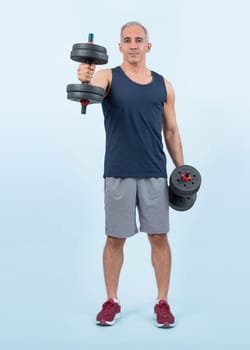 Full body length shot active and sporty senior man lifting dumbbell during weight training workout on isolated background. Healthy active physique and body care lifestyle for pensioner. Clout