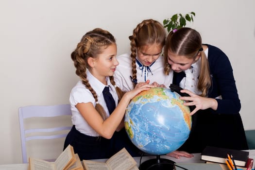 three girls with books and a globe in class at the desk