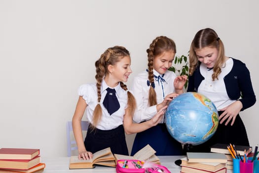 three girls with books and a globe in class at the desk