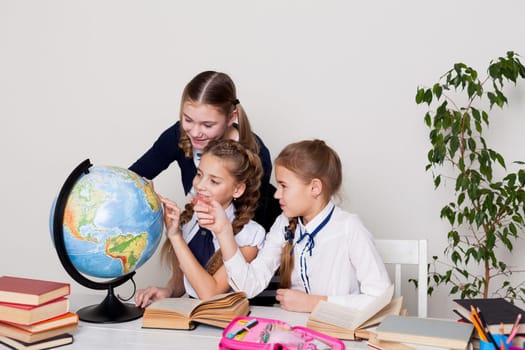 three girls with books and a globe in class at the desk