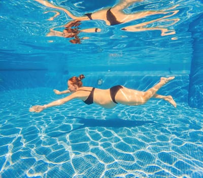 Pregnant serenity submerged a woman gracefully dives into the pool, celebrating the beauty of pregnancy with aquatic elegance.