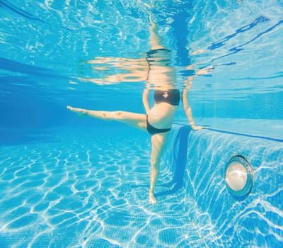 Embracing aquatic fitness, a pregnant woman demonstrates strength and serenity in underwater aerobics, creating a serene and empowering image in the pool.