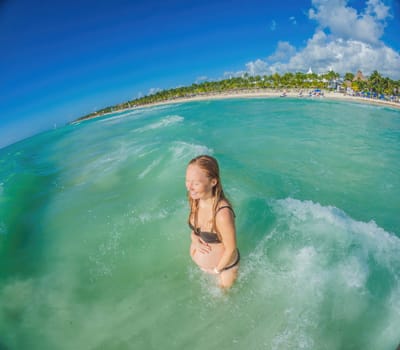 A radiant pregnant woman revels in the serenity of the turquoise sea, embracing the soothing waves as she celebrates the beauty of impending motherhood.