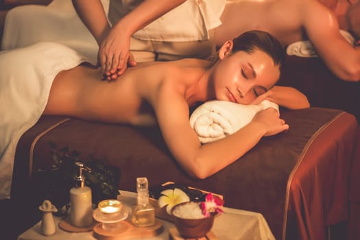 Caucasian couple customer enjoying relaxing anti-stress spa massage and pampering with beauty skin recreation leisure in warm candle lighting ambient salon spa at luxury resort or hotel. Quiescent