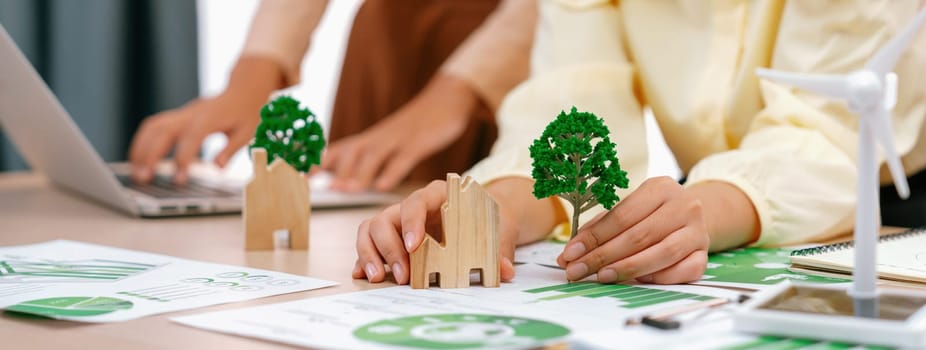 Windmill model represented using renewable energy placed during presenting green business on table with wooden block and environmental document scatter around. Closeup. Delineation.