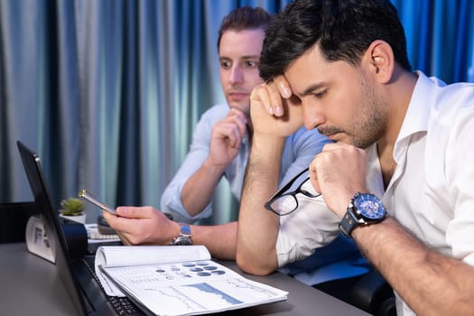 Stressful business partner with headache analyzing paperwork project together on desk at night time of startup product company. Concept of overworked design on neon blue light modern office. Sellable.