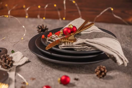 Christmas table with black plates, golden cutlery and holiday decorations.