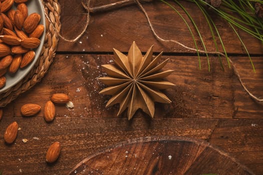 Wooden background with Christmas motifs, a paper star and peeled almonds on a plate